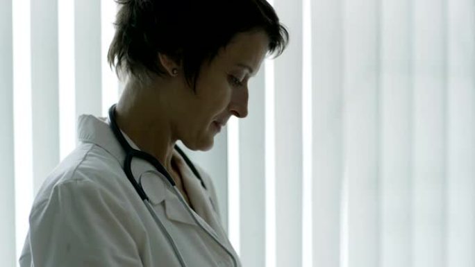穿白大褂的经验丰富的中年女医生浏览平板电脑的俯仰镜头，侧视图