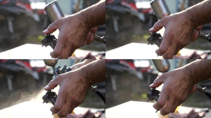 机械师的男性手通过在汽车上喷水来清洗汽车的细节。男人在工作中使用喷雾瓶。修理工在户外工作。背景模糊。