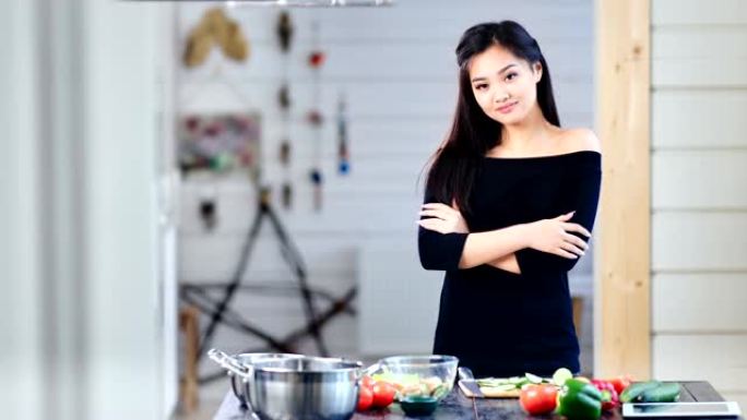 美丽的年轻亚洲女孩在烹饪时双手交叉站着看着相机