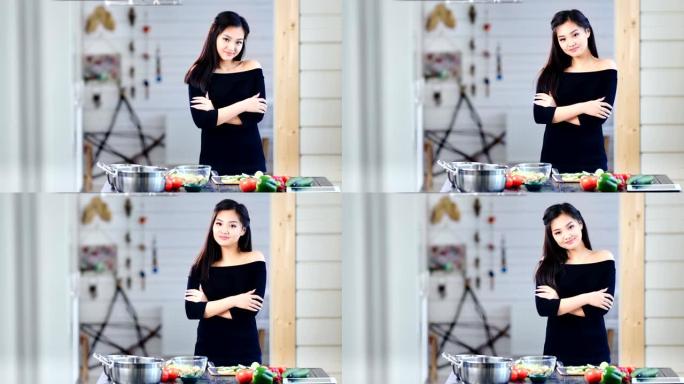 美丽的年轻亚洲女孩在烹饪时双手交叉站着看着相机