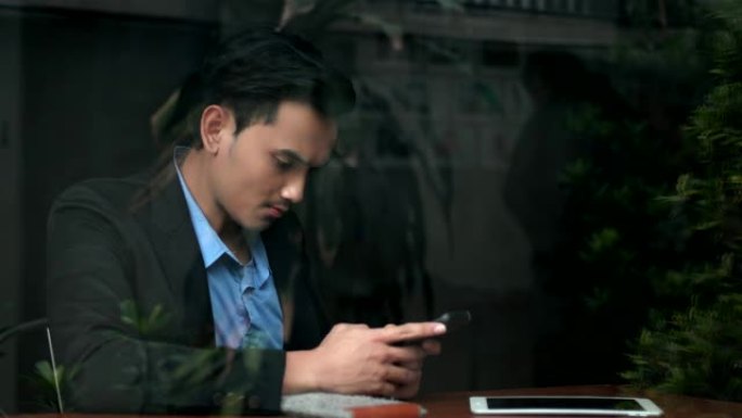 这位年轻的商人在玻璃窗附近使用了智能手机
