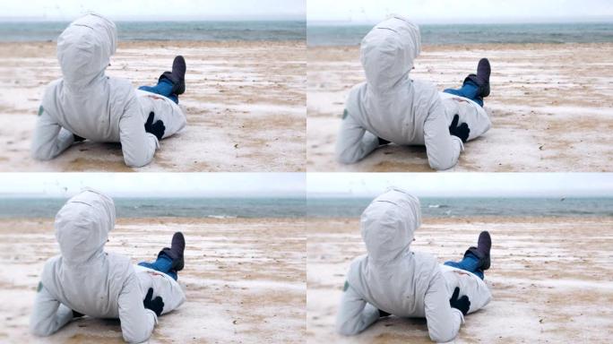 冬季，女游客躺在海边的白雪皑皑的沙滩上。
