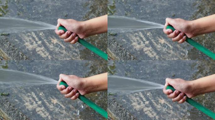 手持花园软管从绿色橡胶管喷水。清洁水泥地板。运动4k镜头