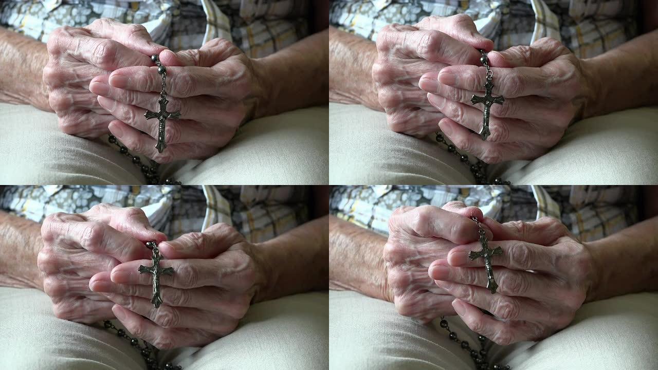 用念珠或耶稣受难像祈祷的高级妇女的手