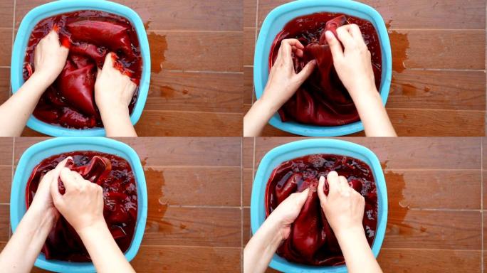 4K。女人用手在盆里洗布，红色衬衫上的红色在水面上流血。颜色运行问题