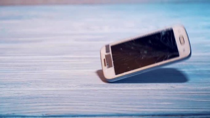 现代白色触摸屏手机掉在地板上，坠毁在木质背景地板上。