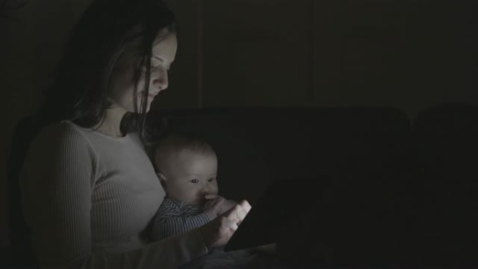 母亲和婴儿在黑暗的房间里使用平板电脑