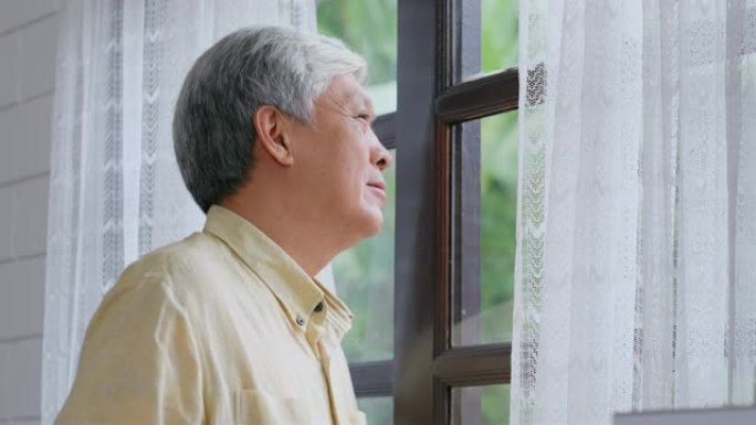 资深亚洲男子站在窗边喝咖啡时情绪放松，退休日常生活方式