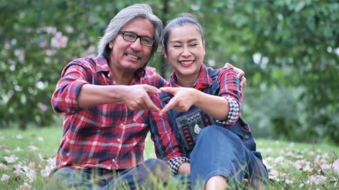亚洲高级夫妇微笑快乐心形手工制作在花园。爱情，浪漫，生活方式，健康理念