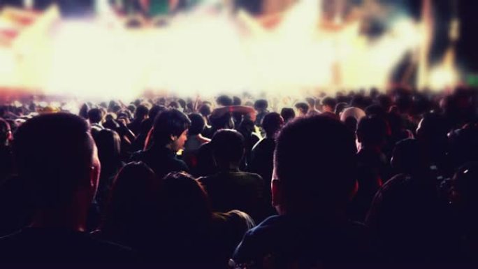 节日人群后视音乐会人群的剪影在明亮的舞台灯光上举手