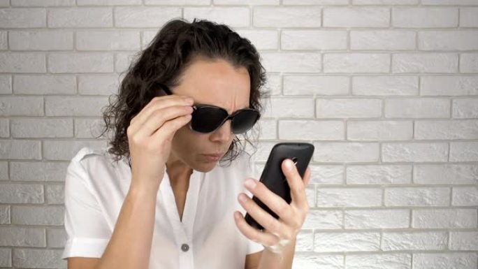 使用智能手机时使用针孔眼镜的女人。眼部护理。