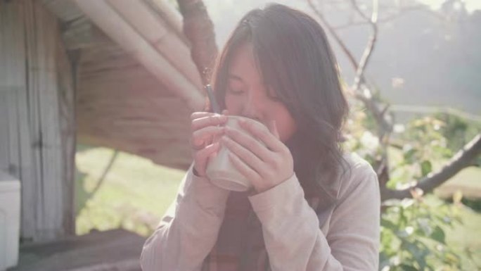 年轻女子早上在家门口的野餐桌上喝热咖啡。
