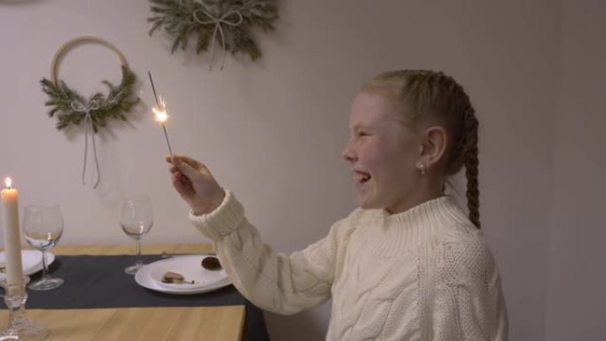 微笑的女孩少年手持明亮的烟火坐在圣诞餐桌上