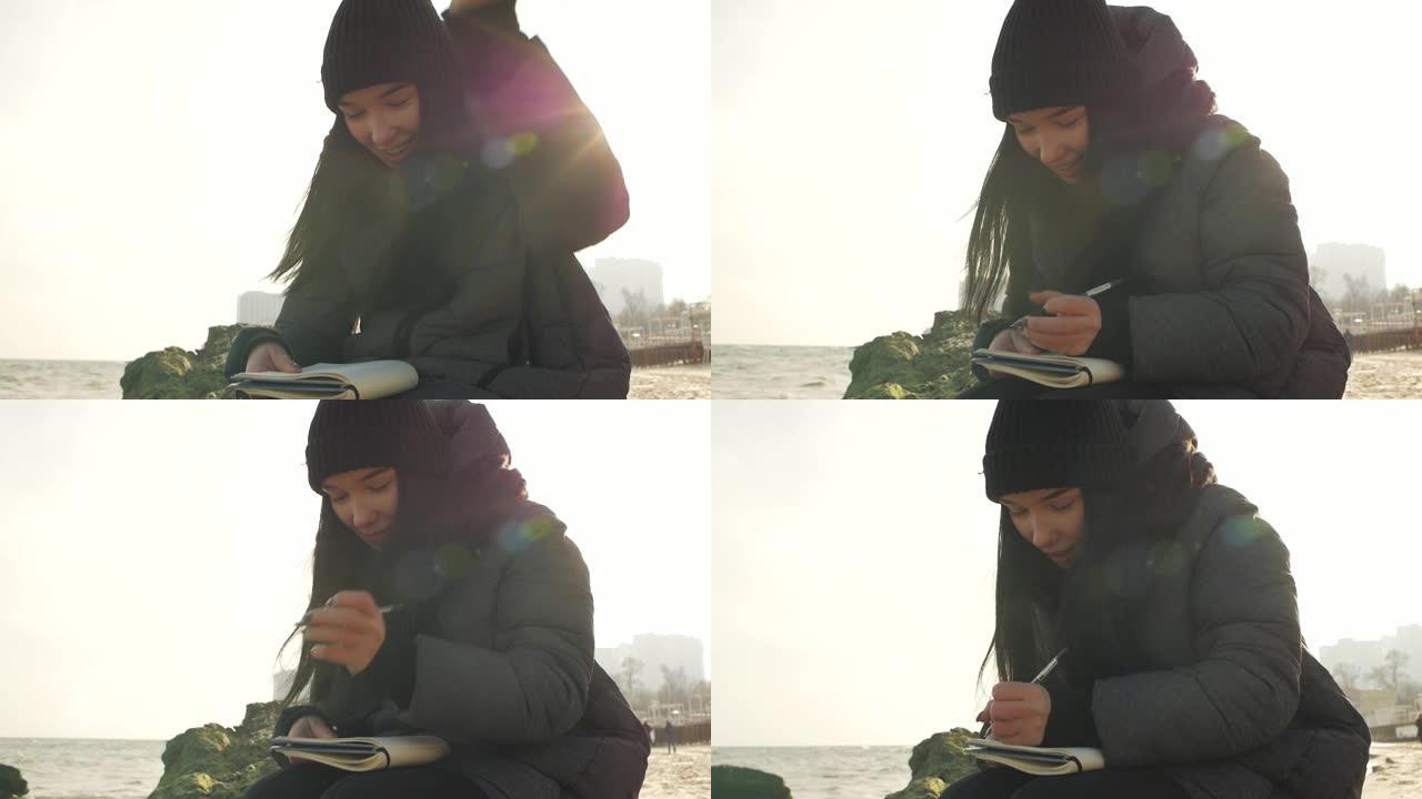 女孩微笑着准备用笔在笔记本上写字坐在海边的一块石头上