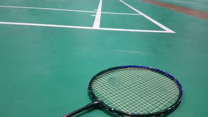 在羽毛球场上，绿色地板上的白色羽毛球shuttle球与模糊的运动员