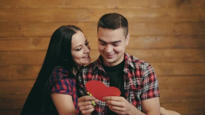 长发女人和她的男朋友调情，他正在用孤立在木制背景上的红心纸雕刻出来。