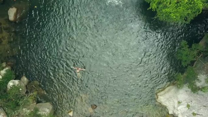 鸟景男子在雨林的山湖游泳。游客在绿色树木和植物之间的野生热带森林的瀑布湖中沐浴。无人机在丛林中查看美