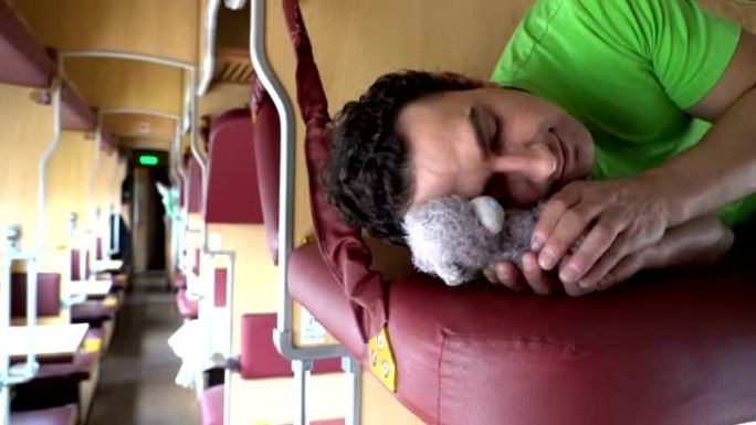 英俊的男人和玩具泰迪熊在火车上睡觉。劳累的工人学生下班后睡觉，辛苦一天，压痛依恋