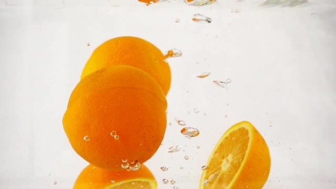 碎裂的橙子迅速沉入水中，带有气泡，慢动作特写