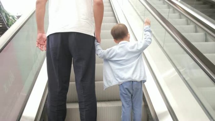 可爱的小亚洲2 -3岁幼儿男婴儿童和爸爸手牵移动自动扶梯的背面