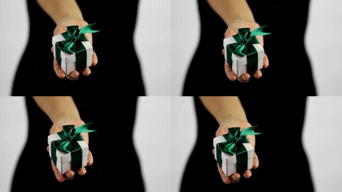 一名妇女正在向相机展示一个带有绿丝带的白色小礼品盒。