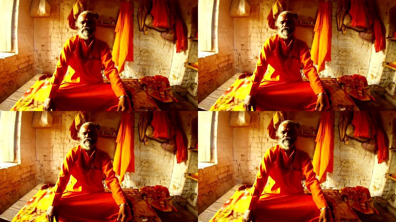 肖像老萨杜印度教僧侣，穿着橙色的衣服，脖子上戴着念珠，房间里有砖砌和墙壁上的衣服