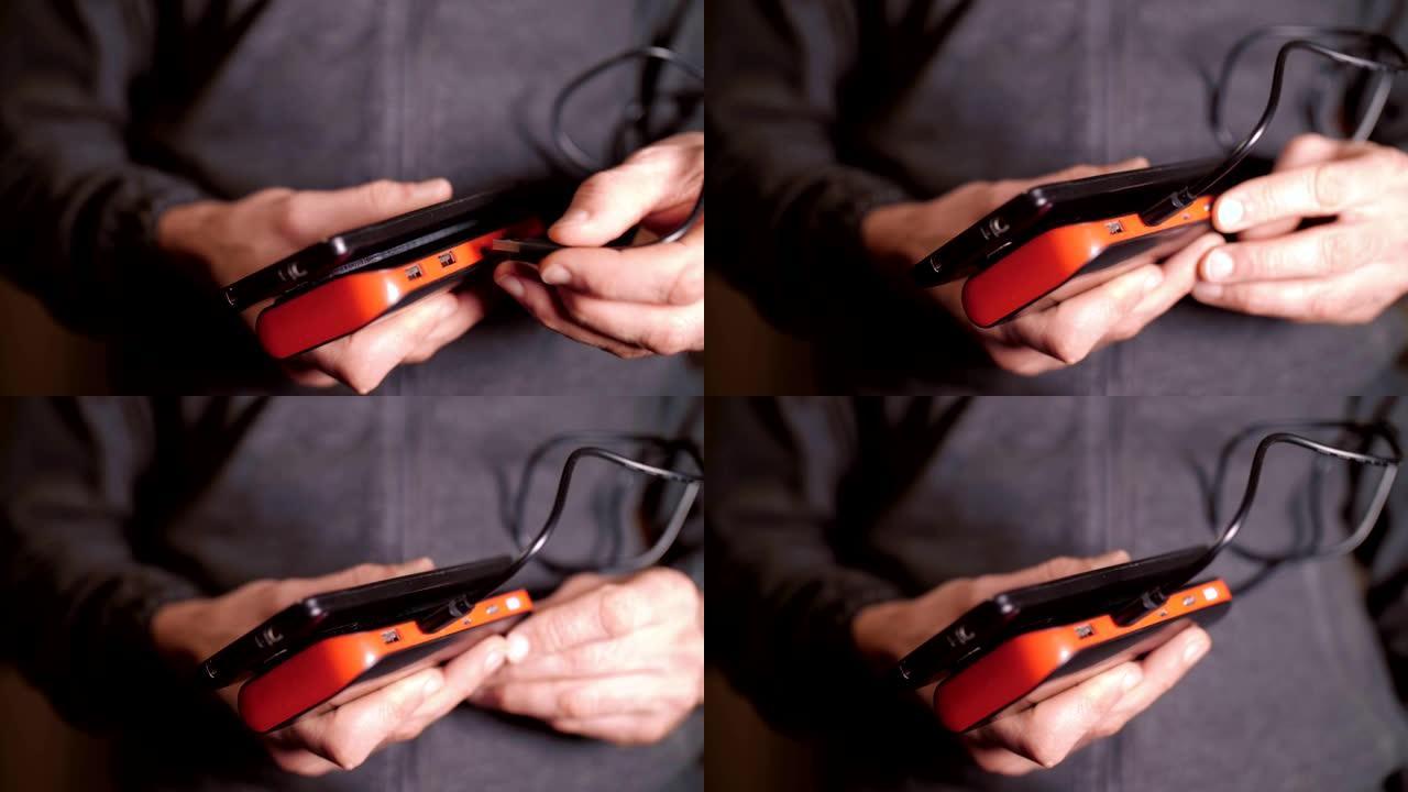 一名男子的手插入USB电缆以连接移动电源和智能手机，为电池充电