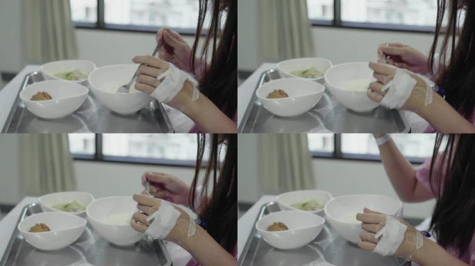 年轻的亚洲女性患者静脉注射溶液在医院病床上吃早餐。