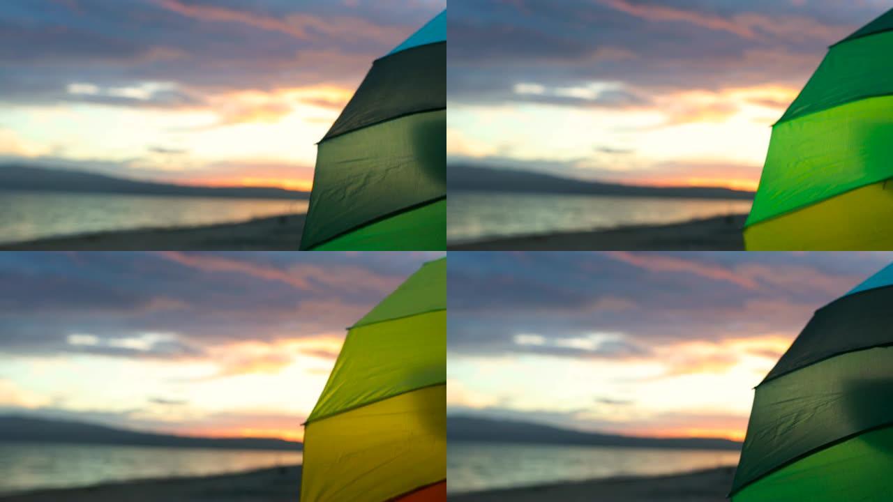 日落时在沙滩上旋转彩虹伞的女人