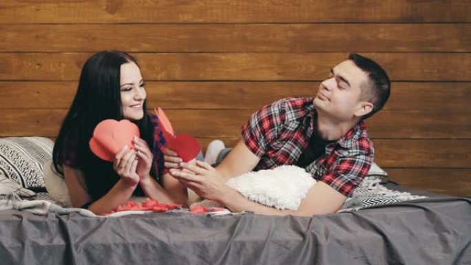 男人拿着三颗纸心给他的女朋友，他们在床上热情地亲吻。