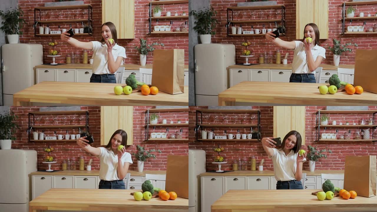 女人在家里厨房用手机浏览。年轻女子在智能手机上浏览微笑快乐。一个女人吃了一个苹果，然后拍照。