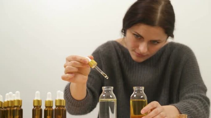 女人用第一瓶的油装满移液器的特写镜头。完整的移液器固定在第二个瓶子上方，水和油滴滴入水中，形成两层