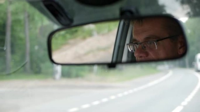 高级男子在乡间小路开车。汽车后视镜中面部的反射。特写