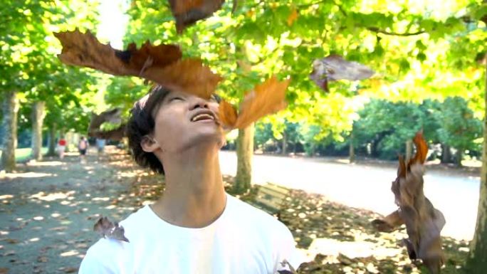 移动万向节射击 -- 快乐微笑的亚洲年轻人在公园扔树叶