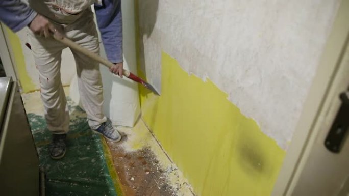 家庭装修，工人用刮刀从混凝土墙上清除旧的黄色油漆