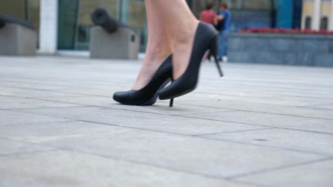 穿着高跟鞋的年轻女商人的脚在城市街道上。穿着黑色鞋子的苗条女性腿穿着高跟鞋走在城市上。女孩踏上工作岗