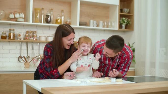 快乐的年轻父母和蹒跚学步的女儿在厨房里玩面粉