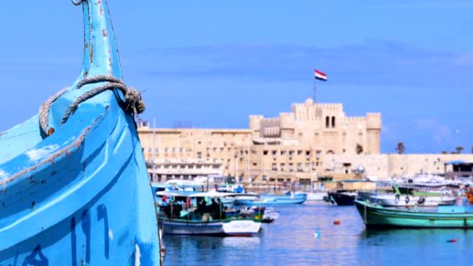 从埃及亚历山大港的地中海俯瞰凯特湾城堡。蓝蓝的天空下，城堡前有很多渔船。