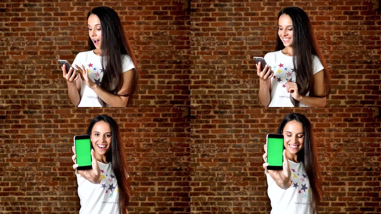 年轻可爱的女孩使用智能手机，令人惊讶，在相机中显示屏幕，色键，背景中的砖墙，肖像