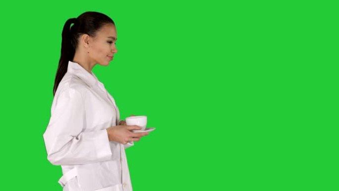 年轻的护士放松喝咖啡或茶，同时走在绿色屏幕上