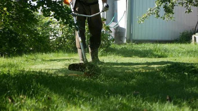 在阳光明媚的夏日，男工人用汽油割草机修剪器用马达割草。在乡下割草。慢动作