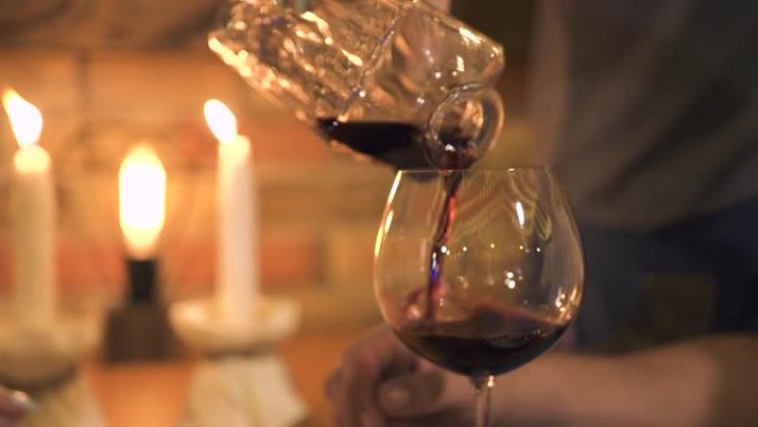 女服务员在餐厅用蜡烛浪漫晚餐时，将红酒倒入玻璃杯中。女服务员在豪华餐厅的晚餐中从酒杯酒瓶中倒酒