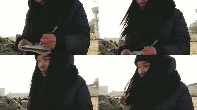 戴着针织帽的海边漂亮女孩用笔在笔记本上写字