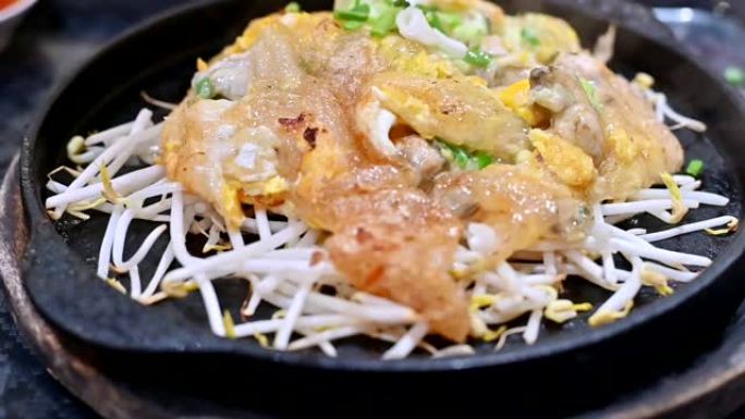 在餐厅提供的热盘中关闭泰国菜或街头小吃的慢动作镜头。炒牡蛎配面粉和豆芽，放在热盘中。