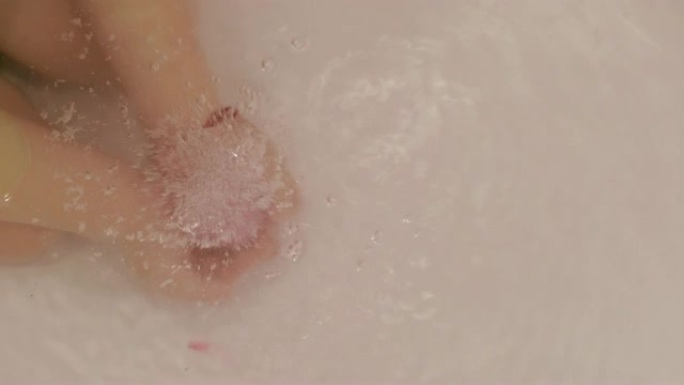 小女孩的手把沐浴炸弹放到水里。沐浴盐球溶解在儿童手中的水中