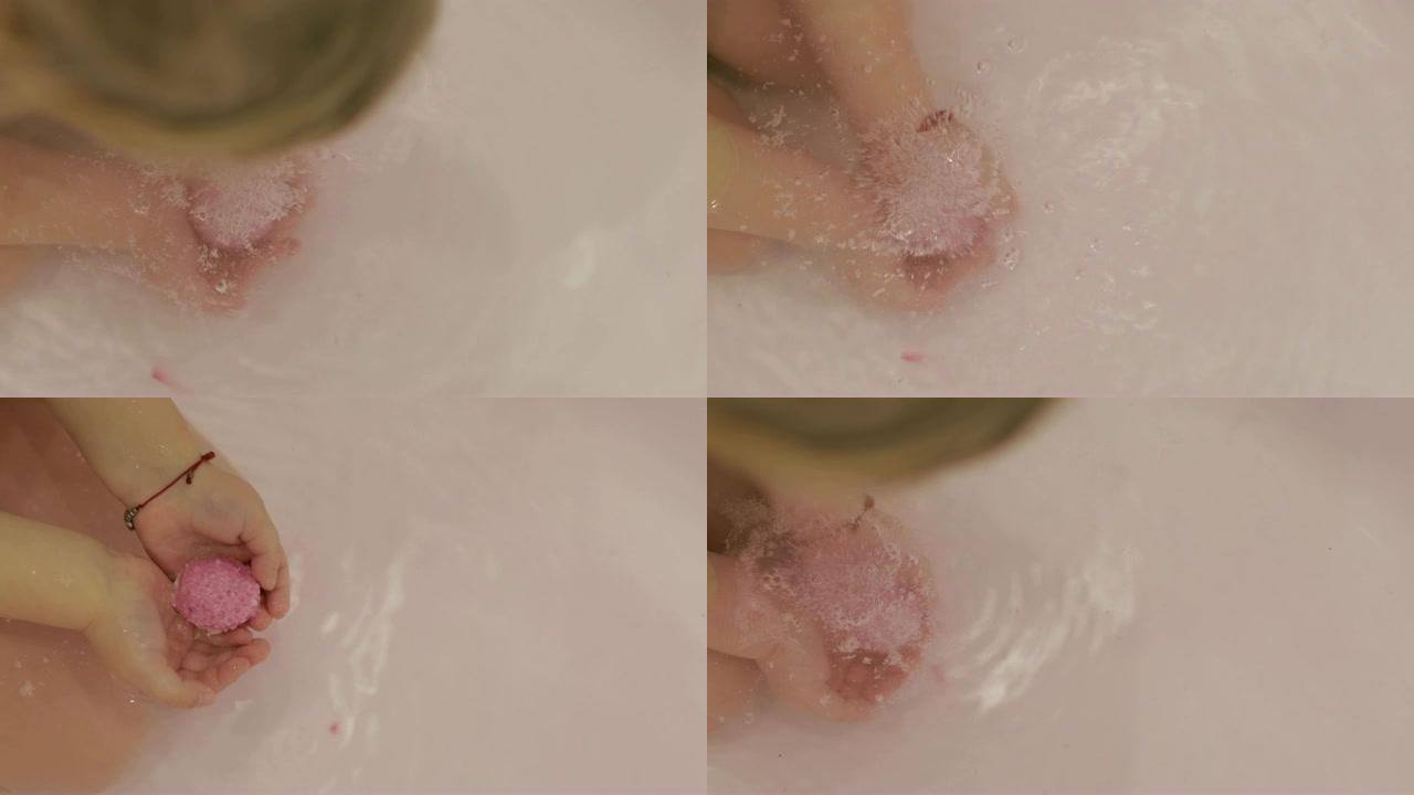 小女孩的手把沐浴炸弹放到水里。沐浴盐球溶解在儿童手中的水中