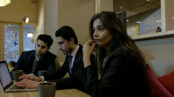 年轻的印度同事在非正式的凉爽多彩的餐厅和共同工作的空间中进行讨论，并在笔记本电脑上不懈地努力工作，需