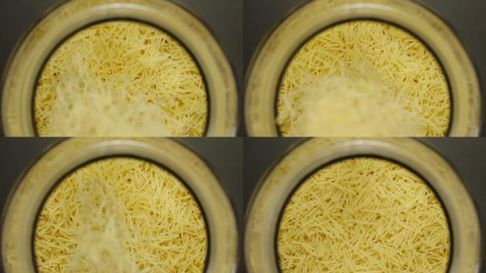 顶视图: 未煮熟的filini意大利面落入黑色背景的玻璃罐中-慢动作