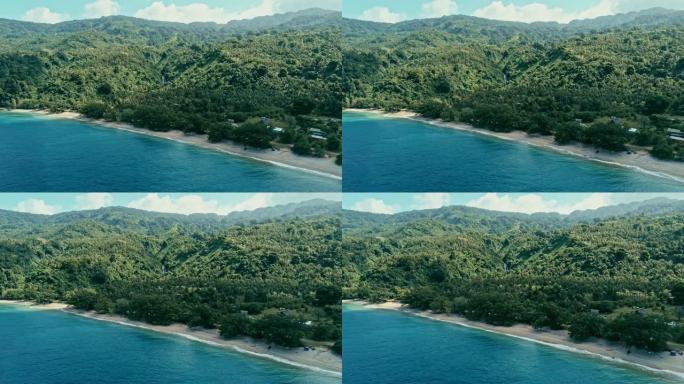 航拍无人机图像的一个偏远岛屿上的一个南太平洋村庄，有着沙滩海岸和郁郁葱葱的热带雨林丛林，背景是瀑布