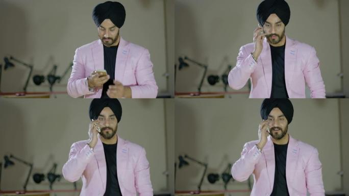 锡克教徒男子穿着淡粉色西装，穿着时髦的衣服，用他的智能手机打了个电话